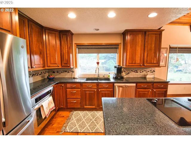 a kitchen with stainless steel appliances granite countertop a refrigerator a sink dishwasher a stove with wooden cabinets and floor