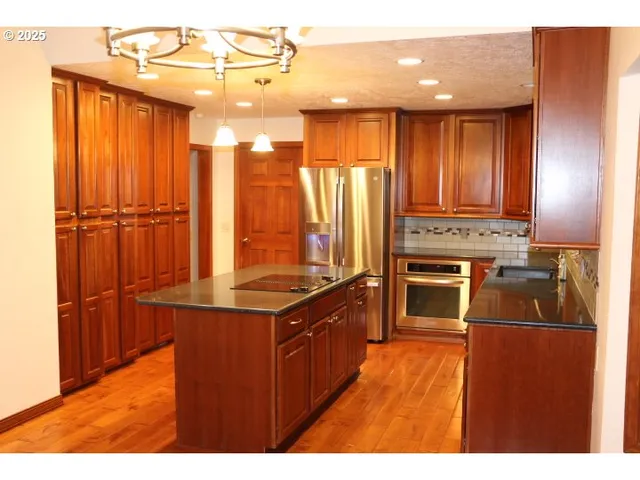 a kitchen with stainless steel appliances granite countertop a stove a sink and a refrigerator with wooden floor