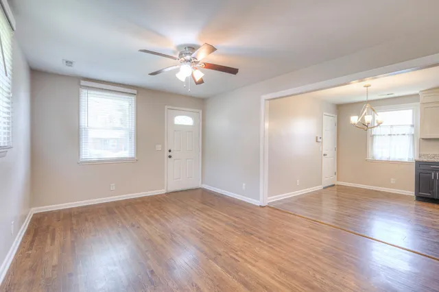 an empty room with wooden floor chandelier fan and windows