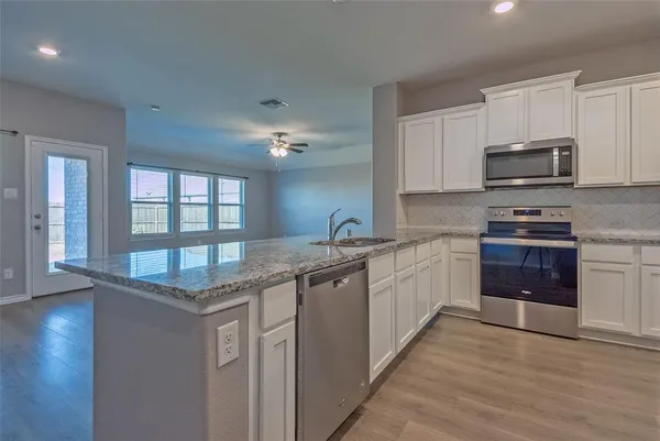 a kitchen with kitchen island granite countertop a stove top oven a sink and dishwasher with wooden floor