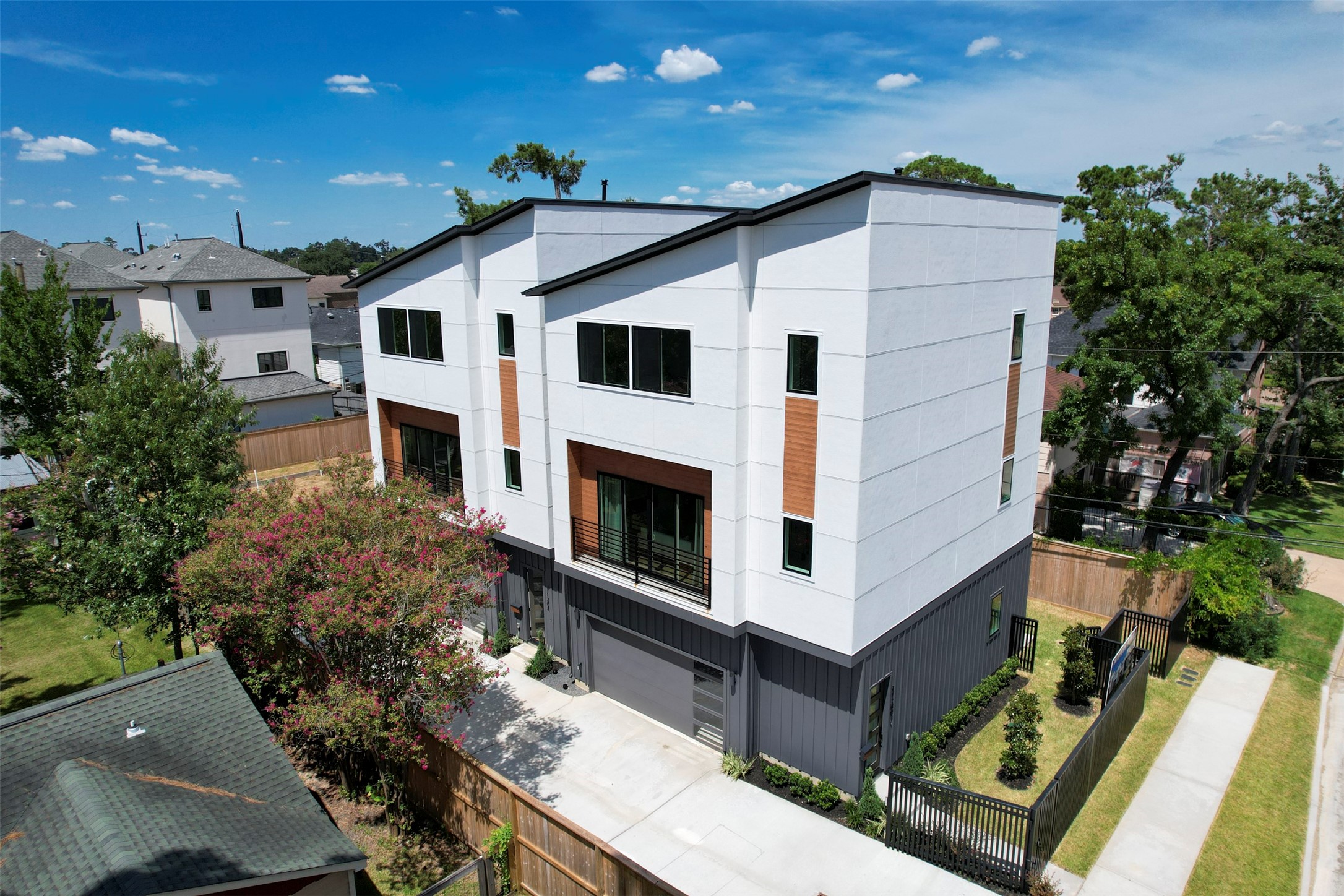 Modern three-story townhouse with a sleek design, featuring large windows, a two-car garage, and a spacious driveway. The exterior combines wood accents with contemporary finishes, offering a clean and stylish look. Notice the huge side and back yard perfect for pets.