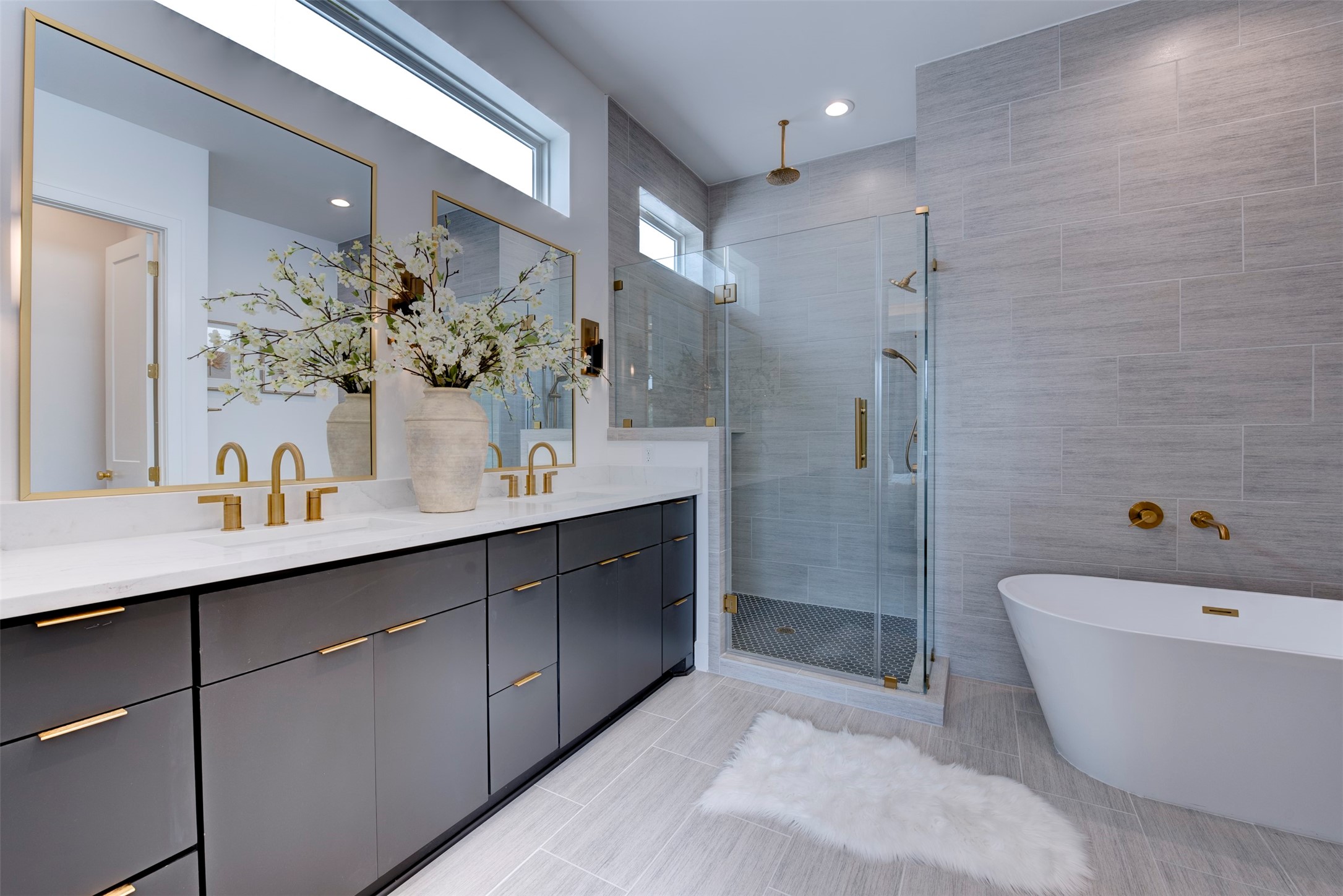 7120 Gary Street, Unit B Houston, TX 77055 - Photo 22 of 29 This modern bathroom features a sleek glass-enclosed shower with gold fixtures, a freestanding bathtub, light gray tiles, and elegant decor, offering a luxurious and serene atmosphere.