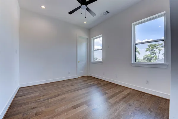 an empty room with wooden floor chandelier fan and windows