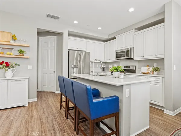 a kitchen with stainless steel appliances granite countertop a refrigerator a sink dishwasher a stove and white countertops with wooden floor