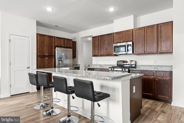 a kitchen with stainless steel appliances granite countertop a stove top oven a sink a refrigerator and chairs