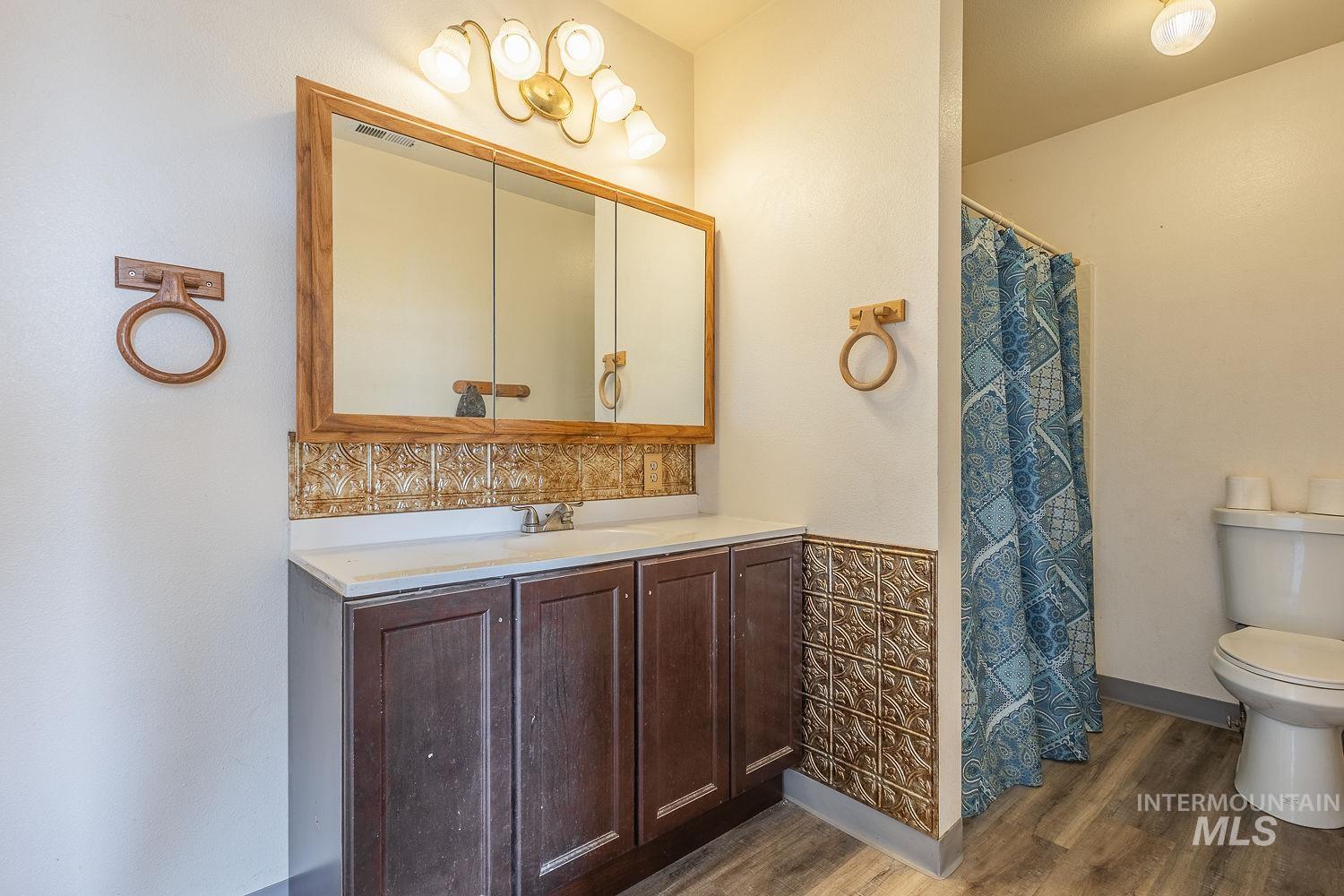 6050 Elmore Road Fruitland, ID 83619 - Photo 17 of 48 Full bathroom with dark wood-style floors, vanity, a shower with shower curtain, wainscoting, and tile walls