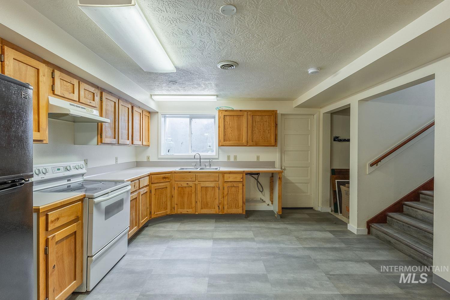 6050 Elmore Road Fruitland, ID 83619 - Photo 29 of 48 Kitchen featuring white range with electric stovetop, freestanding refrigerator, light countertops, under cabinet range hood, and a textured ceiling