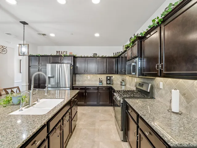 a kitchen with stainless steel appliances granite countertop a sink a stove and a wooden cabinets