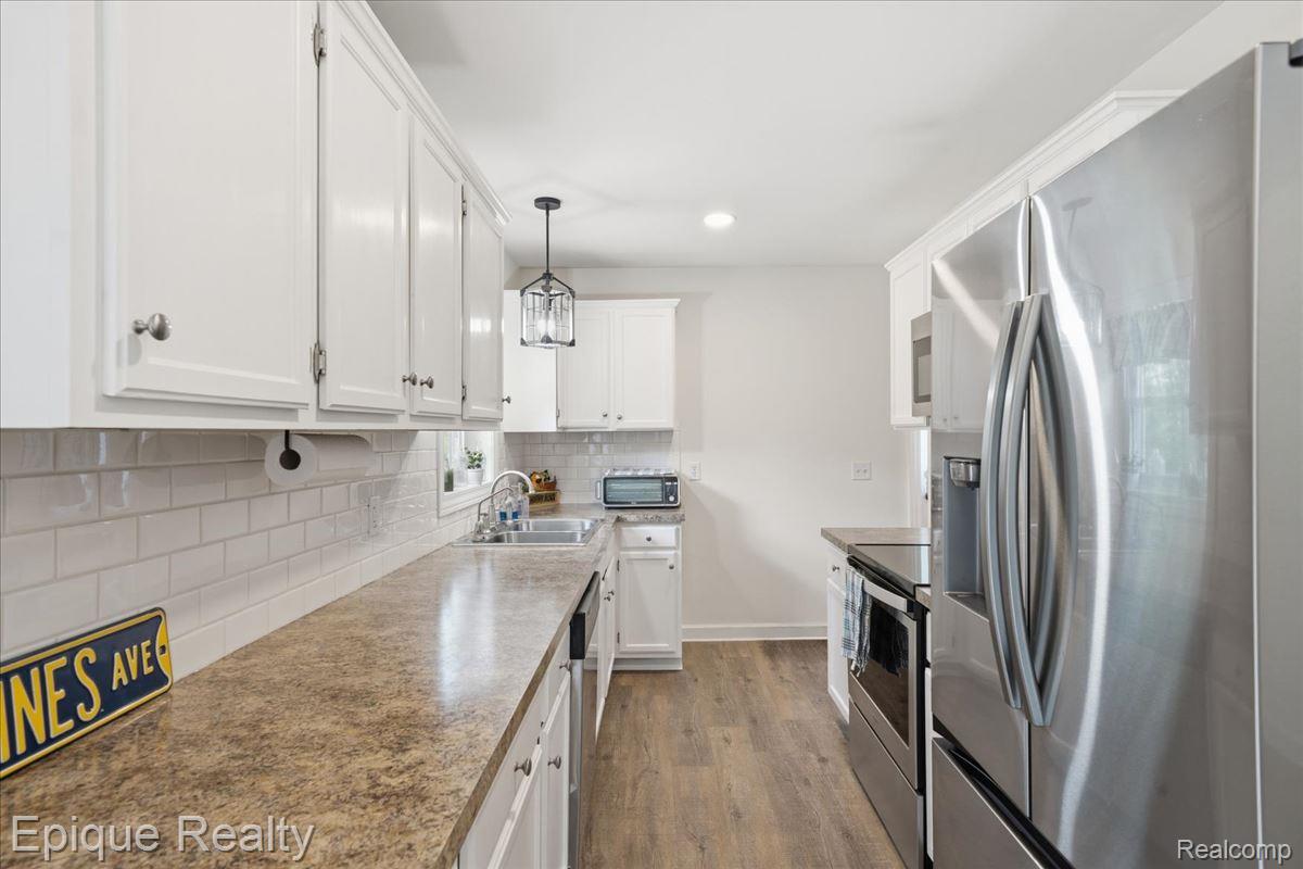 12272 East Mt Morris Road Davison, MI 48423 - Photo 11 of 39 Kitchen featuring wood-finish flooring, white cabinetry, a subway tile backsplash, and stainless steel appliances
