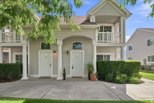 Light-colored siding exterior with a covered entry, upper-level balcony, arched window transoms, and columnar accents