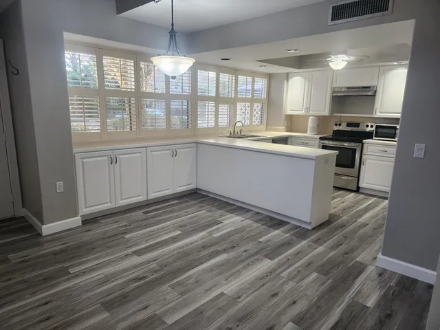 a kitchen with granite countertop a stove a sink and white cabinets with wooden floor