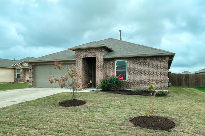 Brick exterior home featuring an attached garage, covered entryway, landscaped front beds, and a fenced side yard
