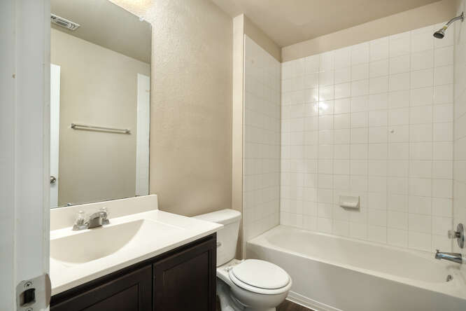 232 Voss Kyle, TX 78640 - Photo 11 of 15 Bathroom featuring a white vanity with integrated sink, dark wood-finish cabinetry, a large wall mirror, and a tiled shower-tub combination with a chrome showerhead