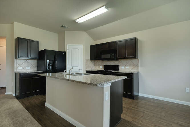 232 Voss Kyle, TX 78640 - Photo 4 of 15 Kitchen featuring dark wood cabinetry, light-toned countertops, and a central island with an integrated sink