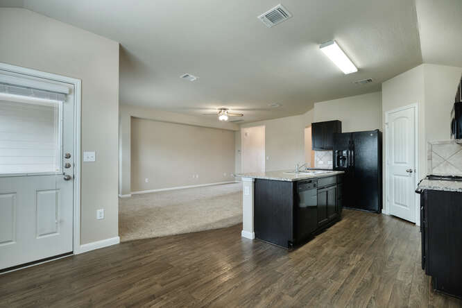 232 Voss Kyle, TX 78640 - Photo 5 of 15 Kitchen featuring wood-finish flooring, dark cabinetry, granite countertops, and a central island with an integrated sink