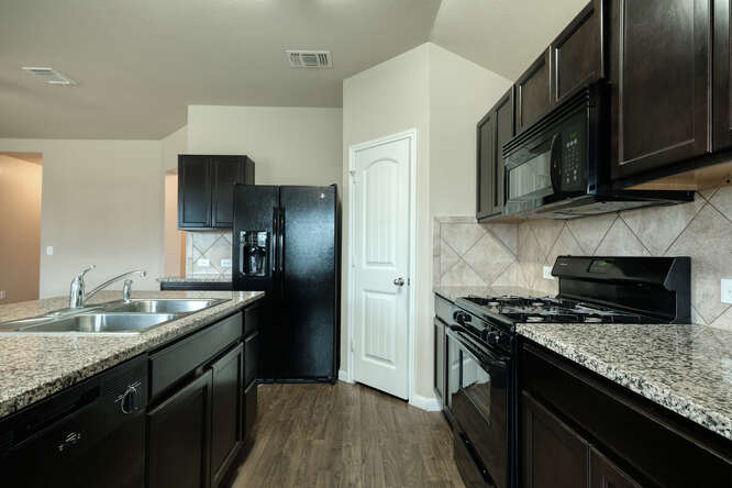 232 Voss Kyle, TX 78640 - Photo 6 of 15 Kitchen featuring granite countertops, dark wood-finish cabinetry, wood-finish flooring, a tile backsplash, and a double basin sink with a chrome faucet