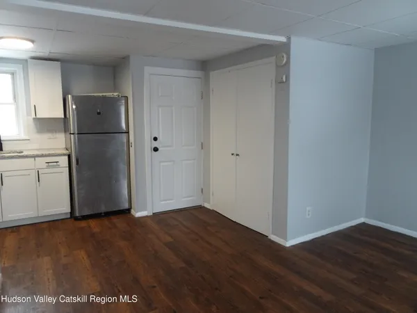 a view of an empty room with wooden floor and a kitchen