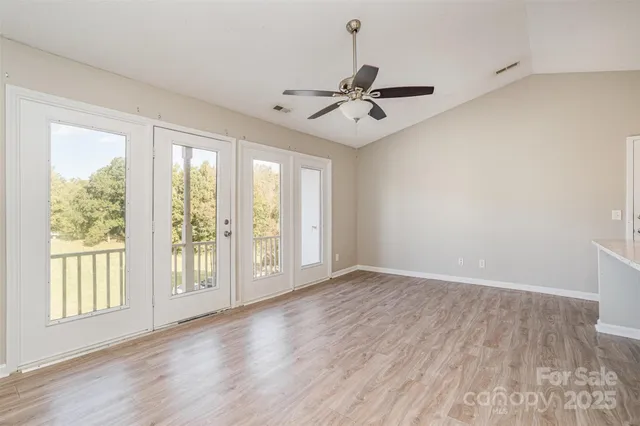 an empty room with wooden floor fan and windows