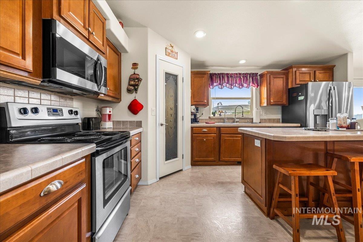 37786 Highway 78 Grand View, ID 83624 - Photo 14 of 50 Kitchen featuring appliances with stainless steel finishes, brown cabinets, a kitchen bar, tile countertops, and recessed lighting