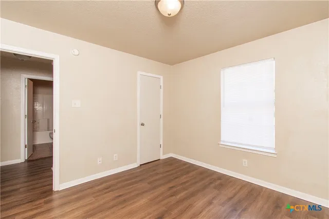 a view of an empty room with wooden floor and a window