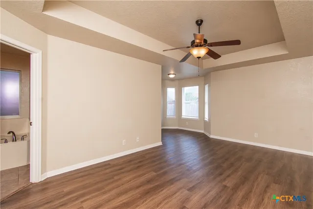 an empty room with wooden floor chandelier fan and windows