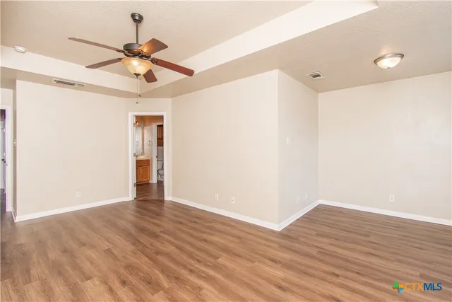 a view of an empty room with wooden floor and a ceiling fan