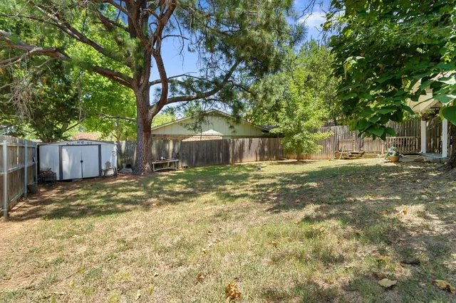 a backyard of a house with large trees and wooden fence