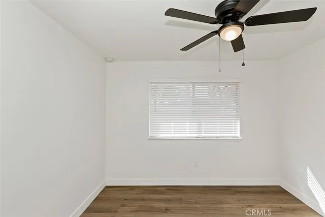an empty room with wooden floor ceiling fan and window