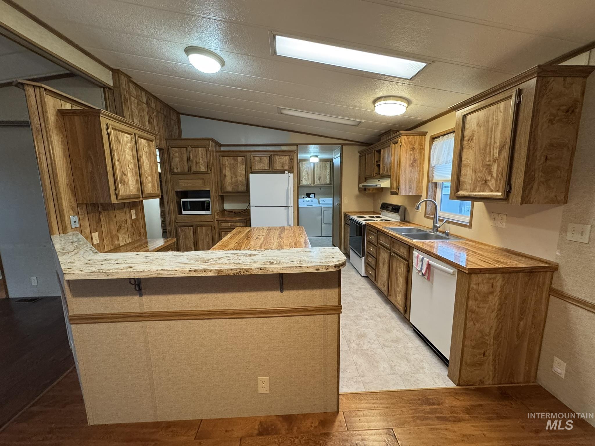2015 6th Avenue, Unit 308 Clarkston, WA 99403 - Photo 9 of 39 Kitchen featuring a peninsula, white appliances, vaulted ceiling, brown cabinets, and light wood-type flooring
