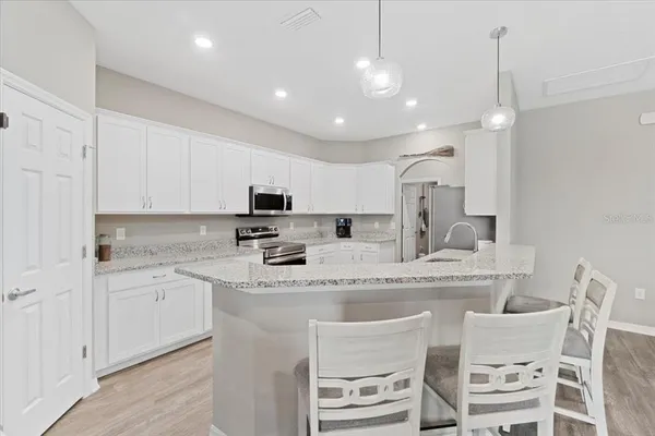 a kitchen with stainless steel appliances granite countertop a sink a stove a refrigerator and white cabinets with wooden floor