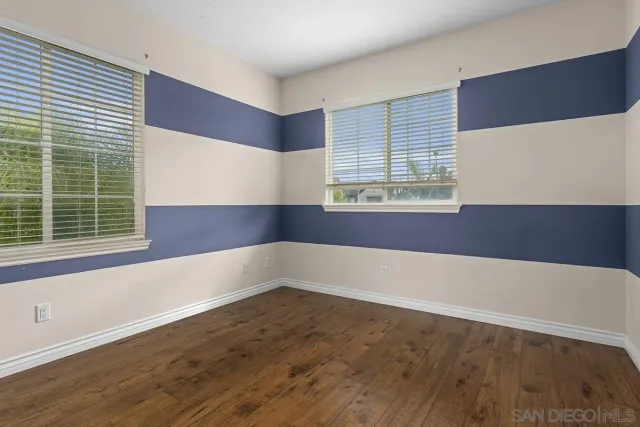an empty room with wooden floor mirror and windows