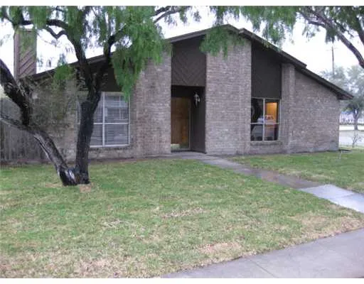 a brick house with a yard plants and large tree
