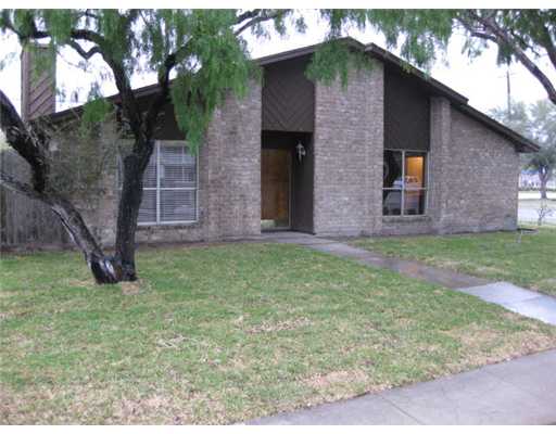 a brick house with a yard plants and large tree