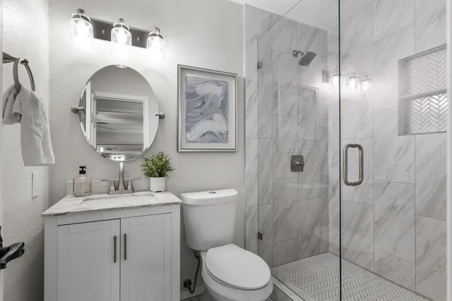 a bathroom with a toilet sink vanity granite and shower