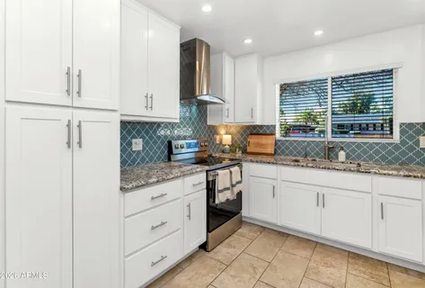 a kitchen with granite countertop white cabinets white appliances a sink and a window