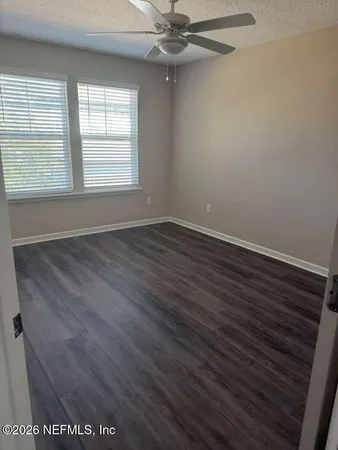 an empty room with wooden floor fan and windows