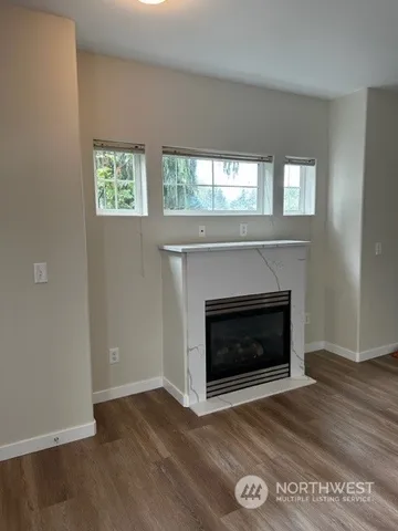 a view of an empty room with wooden floor fireplace and a window