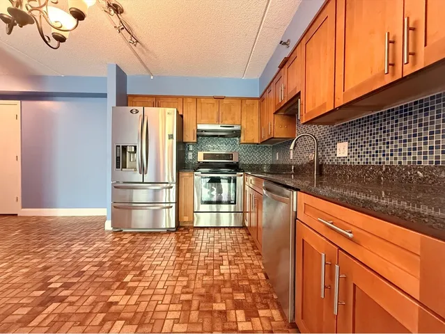 a kitchen with stainless steel appliances granite countertop a refrigerator a stove and a sink with wooden floor