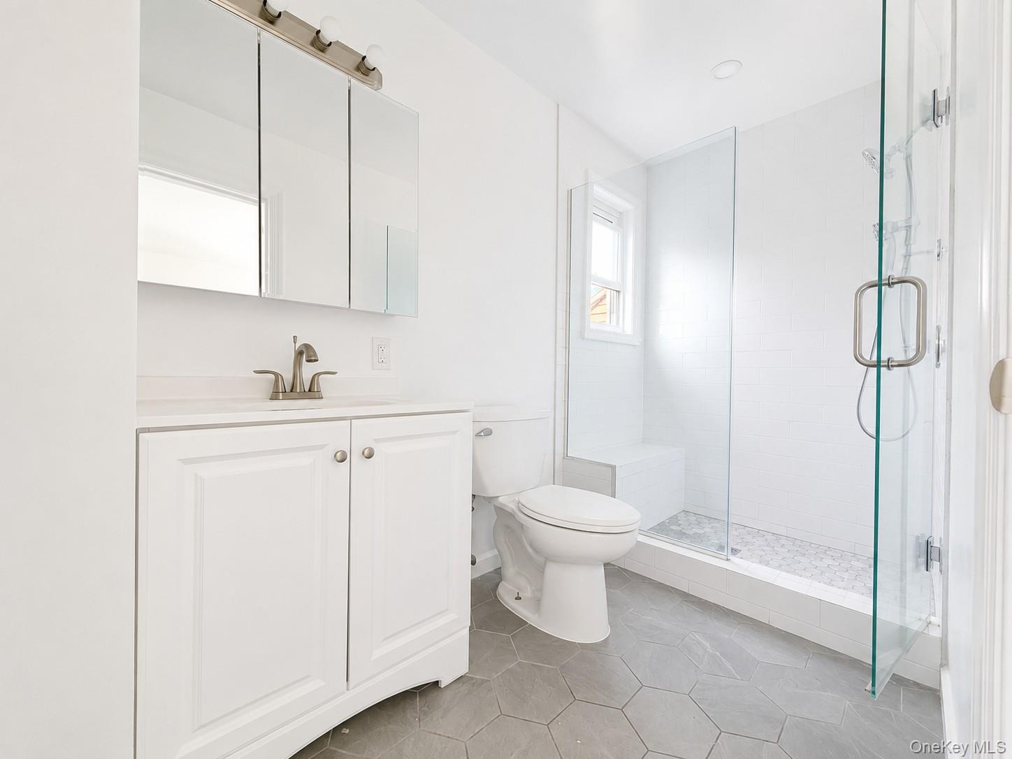25 Monroe Street, Unit 1 Mount Vernon, NY 10550 - Photo 8 of 11 Bathroom featuring a glass-enclosed shower with a built-in bench, hexagon tile flooring, a white vanity with a countertop, a mirrored medicine cabinet, and a window