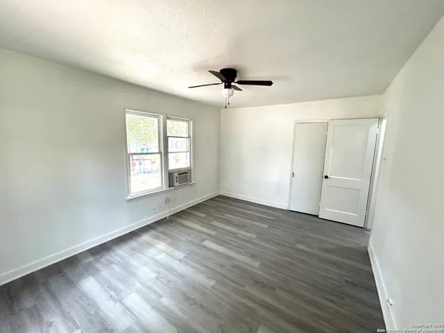 an empty room with wooden floor chandelier fan and windows