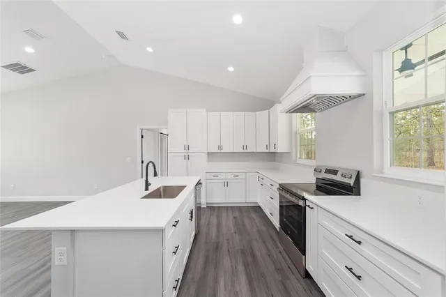 a kitchen with a sink dishwasher a stove and white cabinets with wooden floor
