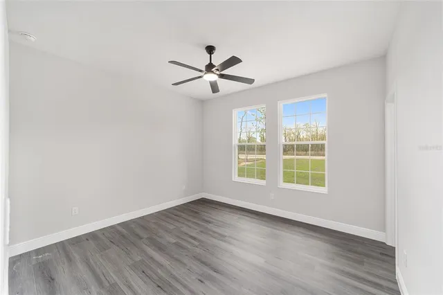 an empty room with wooden floor fan and windows
