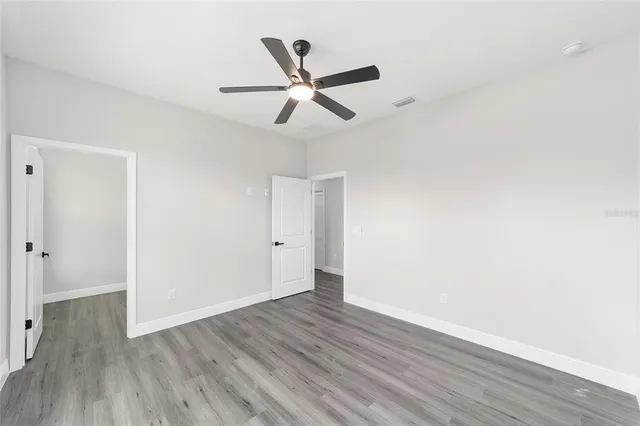 a view of an empty room with wooden floor and a ceiling fan