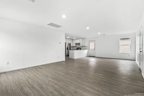 a view of empty room with wooden floor and kitchen