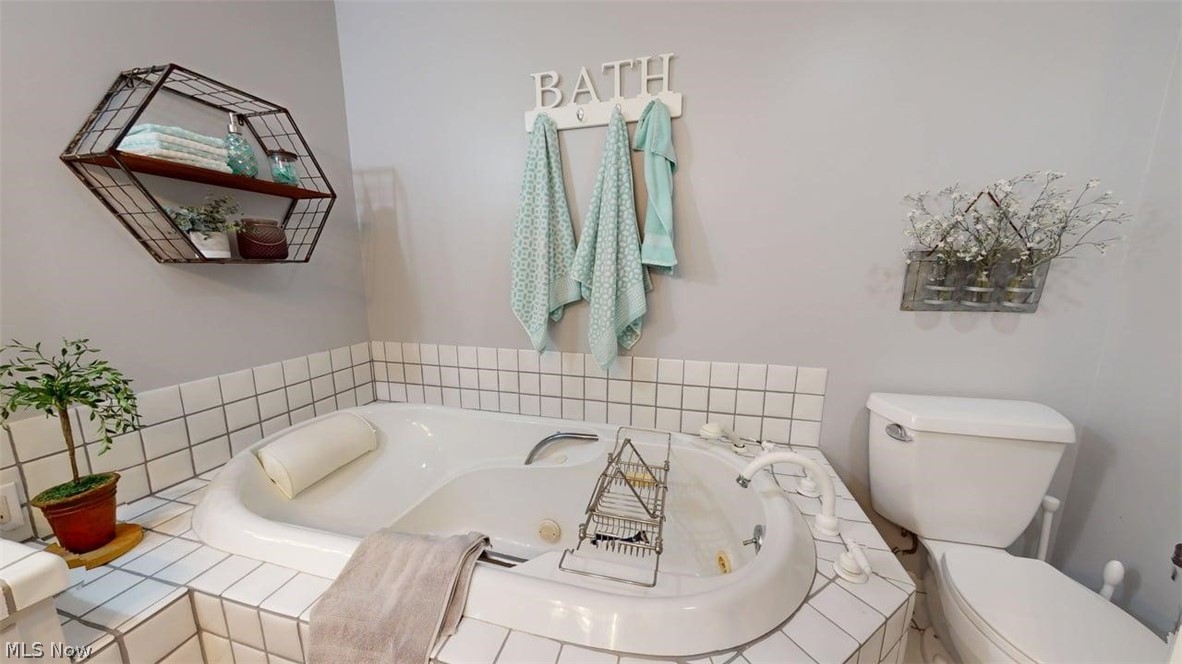 3985 Wiers Road Willard, OH 44890 - Photo 31 of 50 White jetted soaking tub with tiled surround, faucet, and adjacent toilet