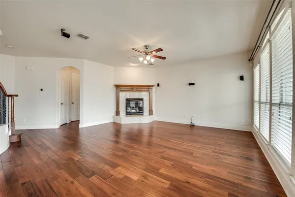 an empty room with wooden floor chandelier fan and windows