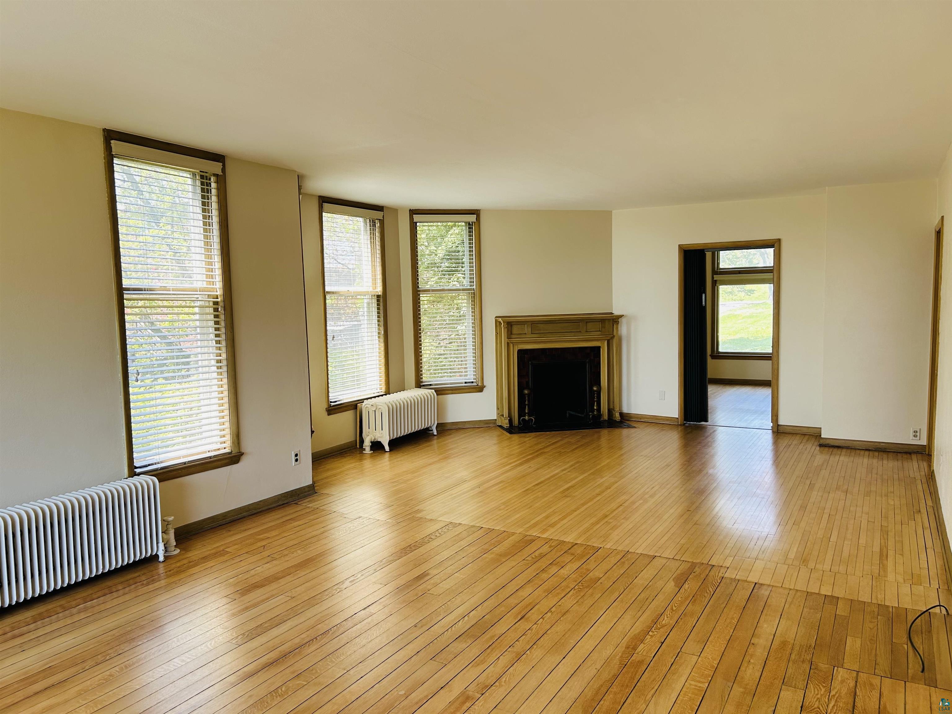 5090 London Road, Unit 1 Duluth, MN 55804 - Photo 27 of 54 Spacious room featuring wood-finish flooring, a decorative fireplace with an ornate mantel, multiple windows with blinds, and classic radiator heating