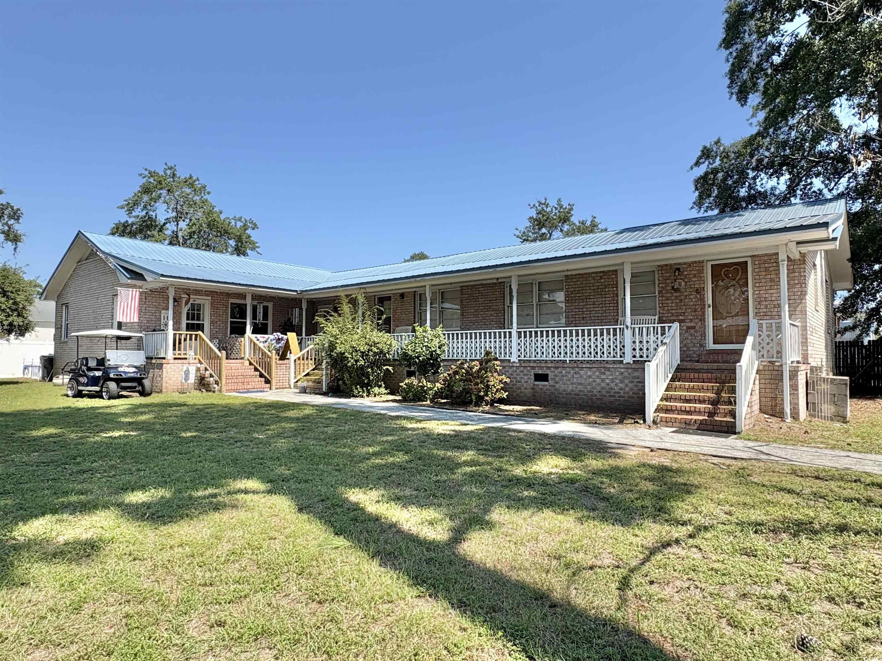 Ranch-style house featuring crawl space, a metal roof, brick siding, covered porch, and a front lawn