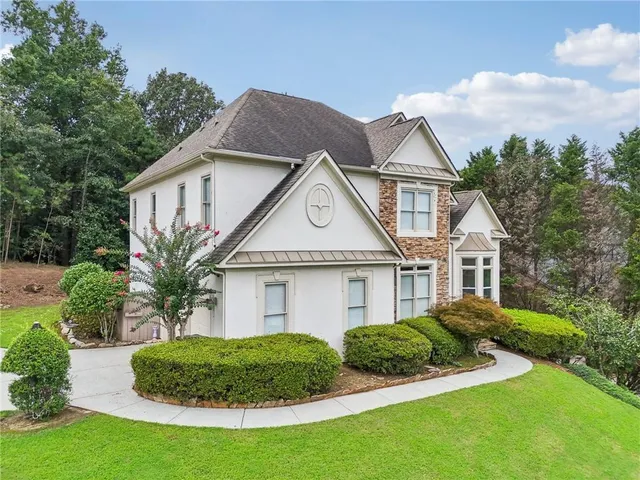 a view of a white house next to a yard with plants and large trees