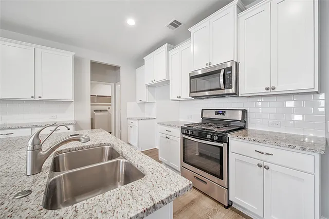 a large kitchen with stainless steel appliances granite countertop a stove a sink dishwasher and a oven with white cabinets